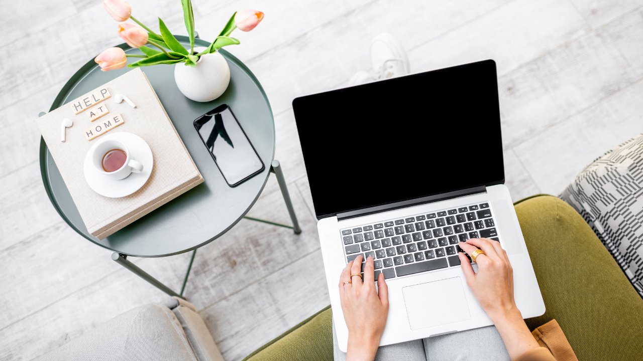 Klant werkt ontspannen op de bank aan haar laptop, met kopje koffie en 'Help at home' bordje op tafel